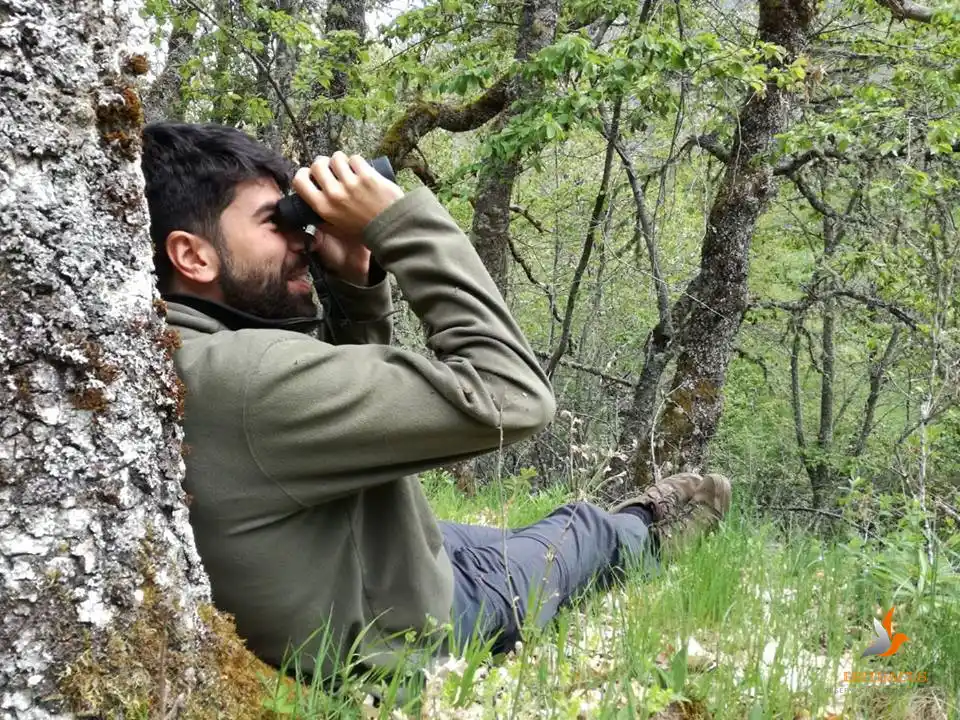 Gonzalo sentado en un bosque observando con unos prismáticos.
